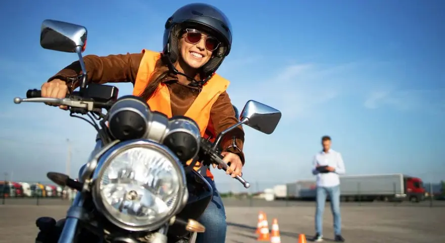 Uśmiechnięta kursantka na motocyklu, gotowa do egzaminu na prawo jazdy kat. A. Sprawdza cenę kursu.