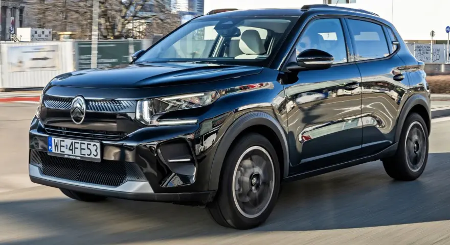 Czarny Citroen C3 porusza się po mieście, odbijając światła i budynki w swojej lśniącej karoserii.