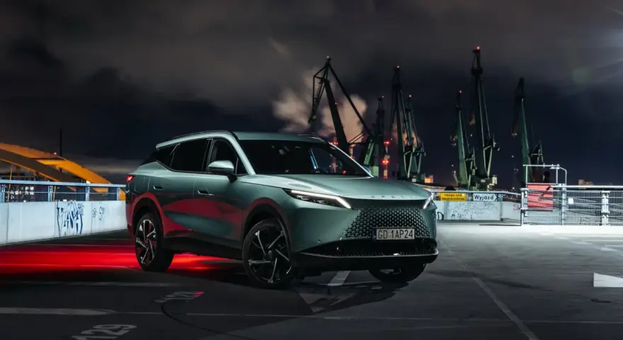 Nowy polski samochód elektryczny Izera na tle nocnego portu z dźwigami.