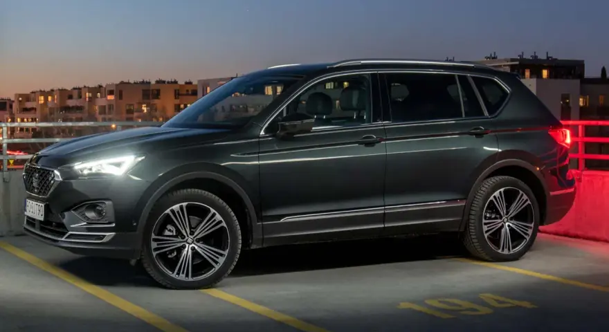 Ciemnozielony SUV z siedmioma miejscami stoi na parkingu nocą, z widokiem na budynki mieszkalne.