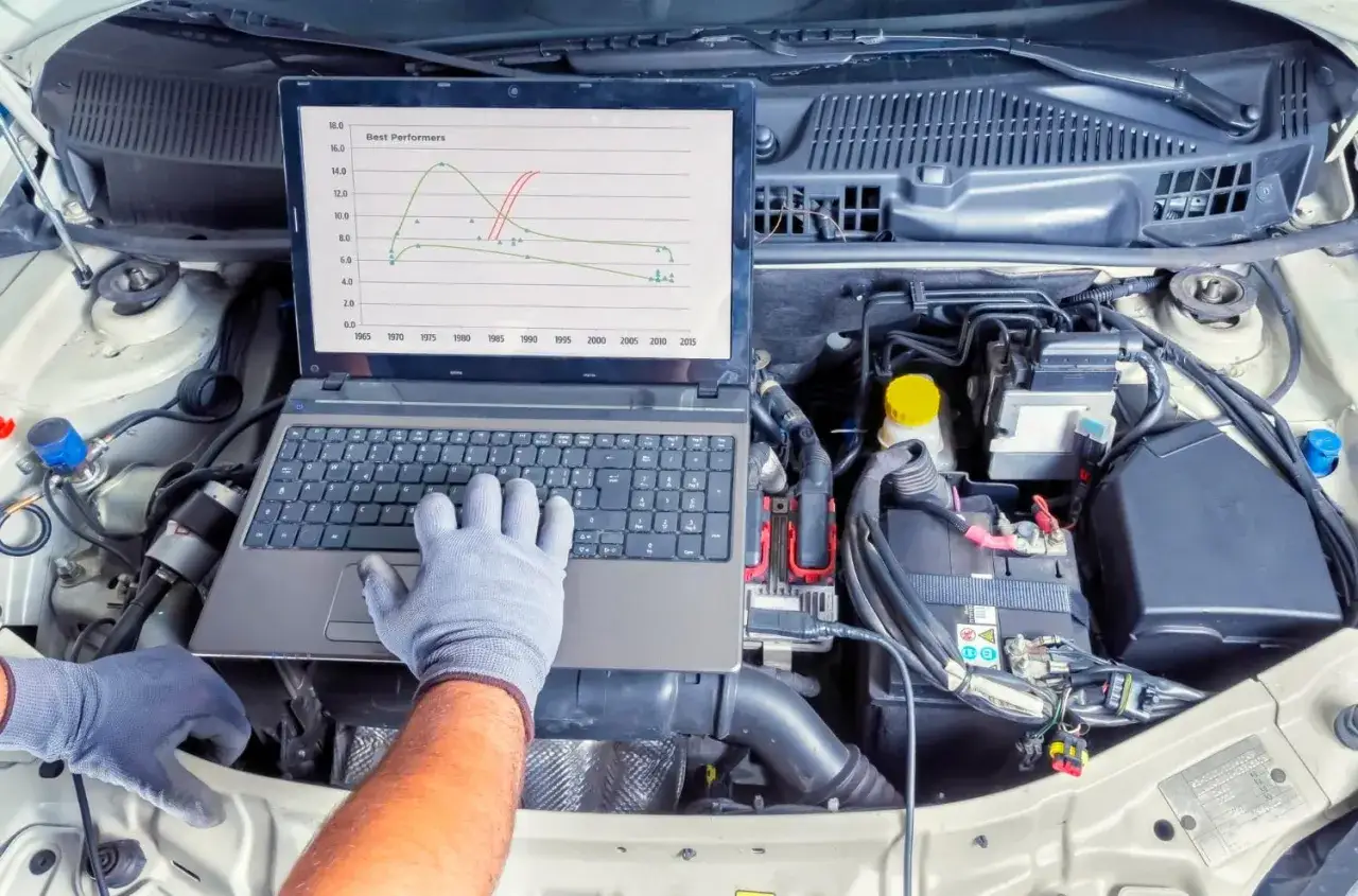 Mechanik diagnozuje kontrolkę silnika, analizując wykres wydajności na laptopie pod maską samochodu.