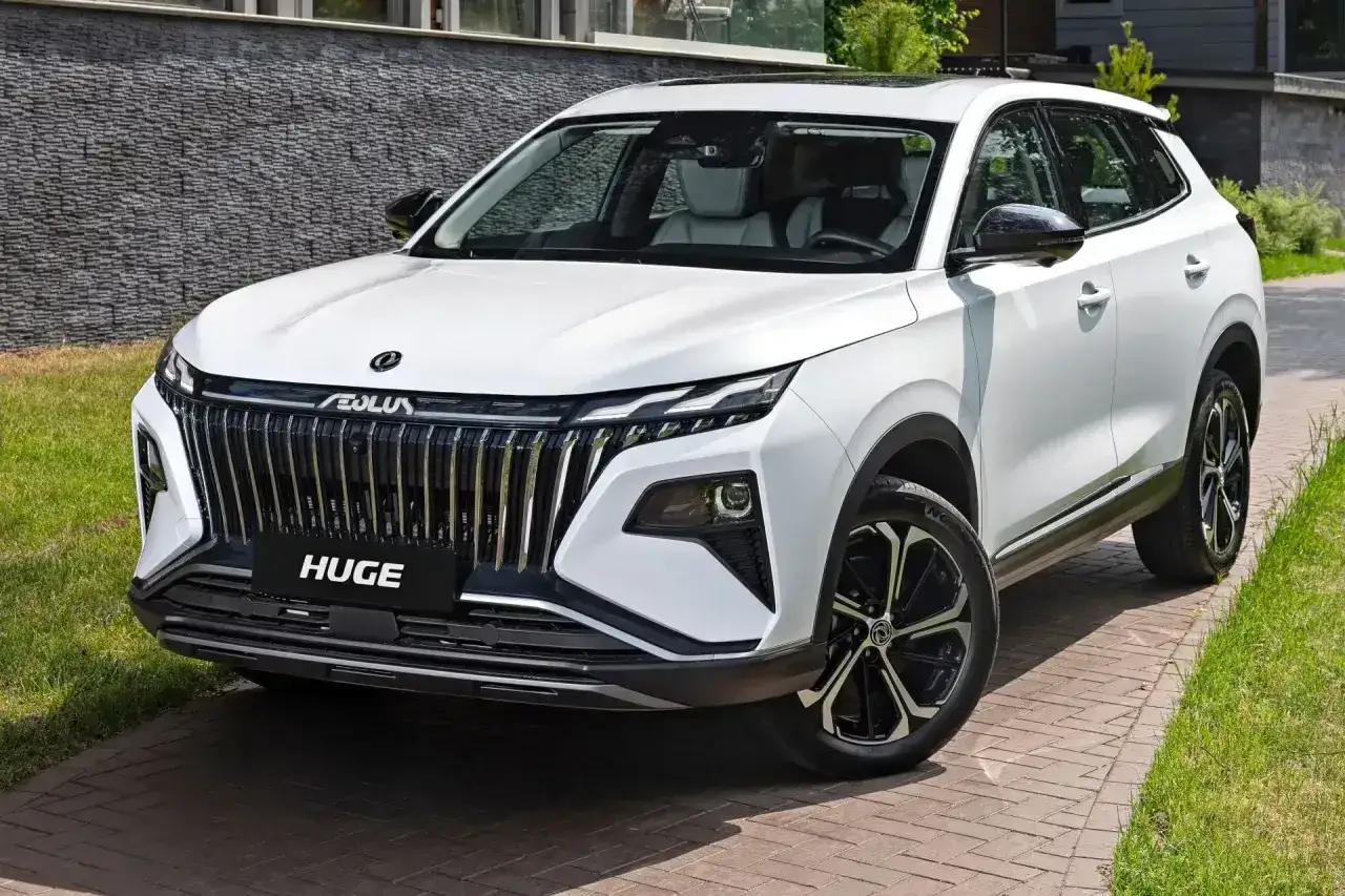 Nowy, biały chinski suv z imponującym grillem i felgami stoi na podjeździe.