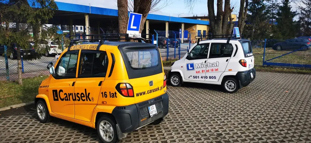 Dwa samochody szkoleniowe, żółty i biały, z literą