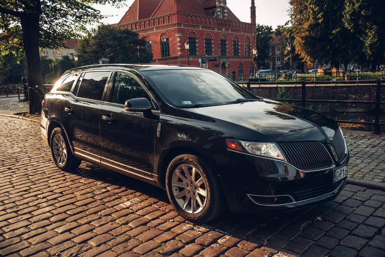 Czarny Lincoln SUV na brukowanej ulicy, z zabytkową ceglaną kamienicą w tle.