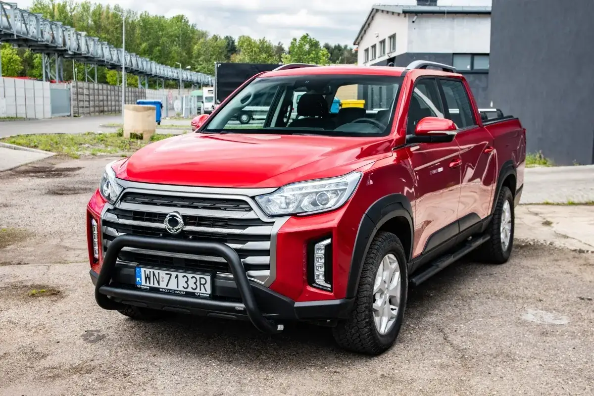 Czerwony SsangYong pickup z czarną osłoną zderzaka i felgami stoi na parkingu.