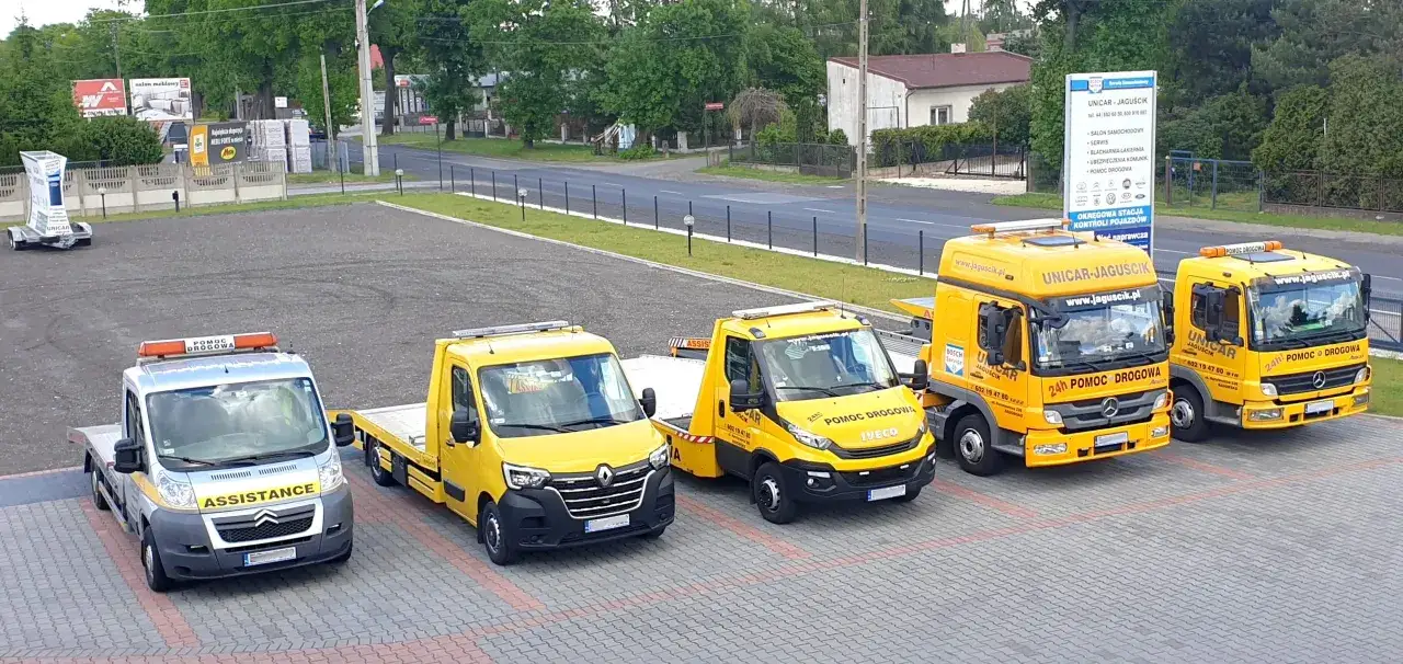 Flota pojazdów pomocy drogowej, w tym jeden srebrny z napisem ASSISTANCE, gotowa do akcji. Warta assistance złoty plus to ich motto.