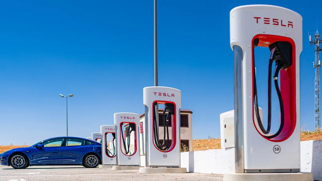 Niebieska Tesla przy ładowarkach. Zastanawiasz się, ile kosztuje Tesla? To zależy od modelu i wyposażenia.