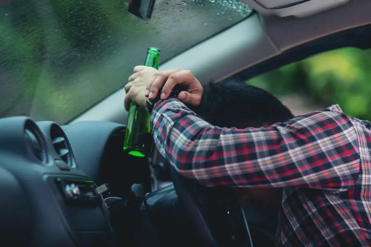 Mężczyzna z butelką piwa w samochodzie. Prowadzenie po alkoholu, nawet 1 promil, grozi utratą prawa jazdy.