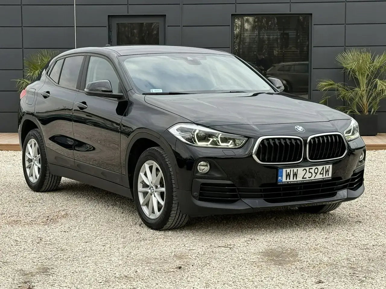 Czarny BMW X2 na żwirowym podjeździe. Sprawdź aktualną bmw x2 cena i dowiedz się więcej o tym stylowym SUV-ie.
