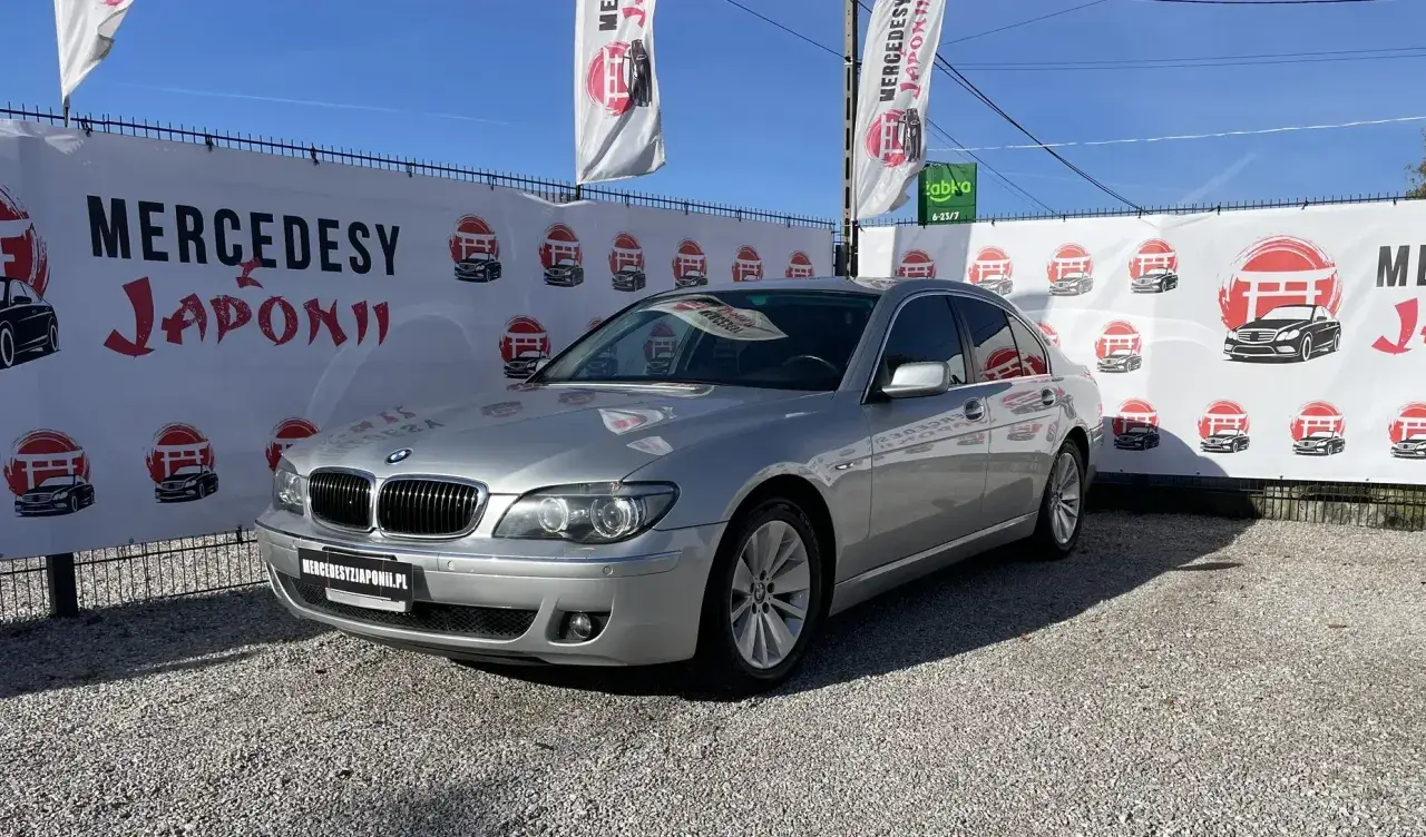 Srebrne BMW 750i na tle baneru z napisem