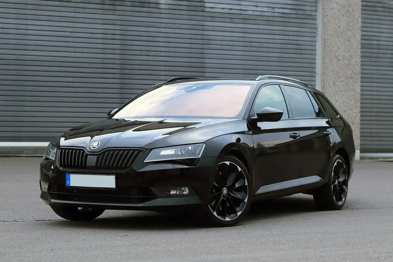 Elegancka, czarna Skoda Combi z przyciemnianymi szybami i czarnymi felgami stoi przed szarą, industrialną bramą.