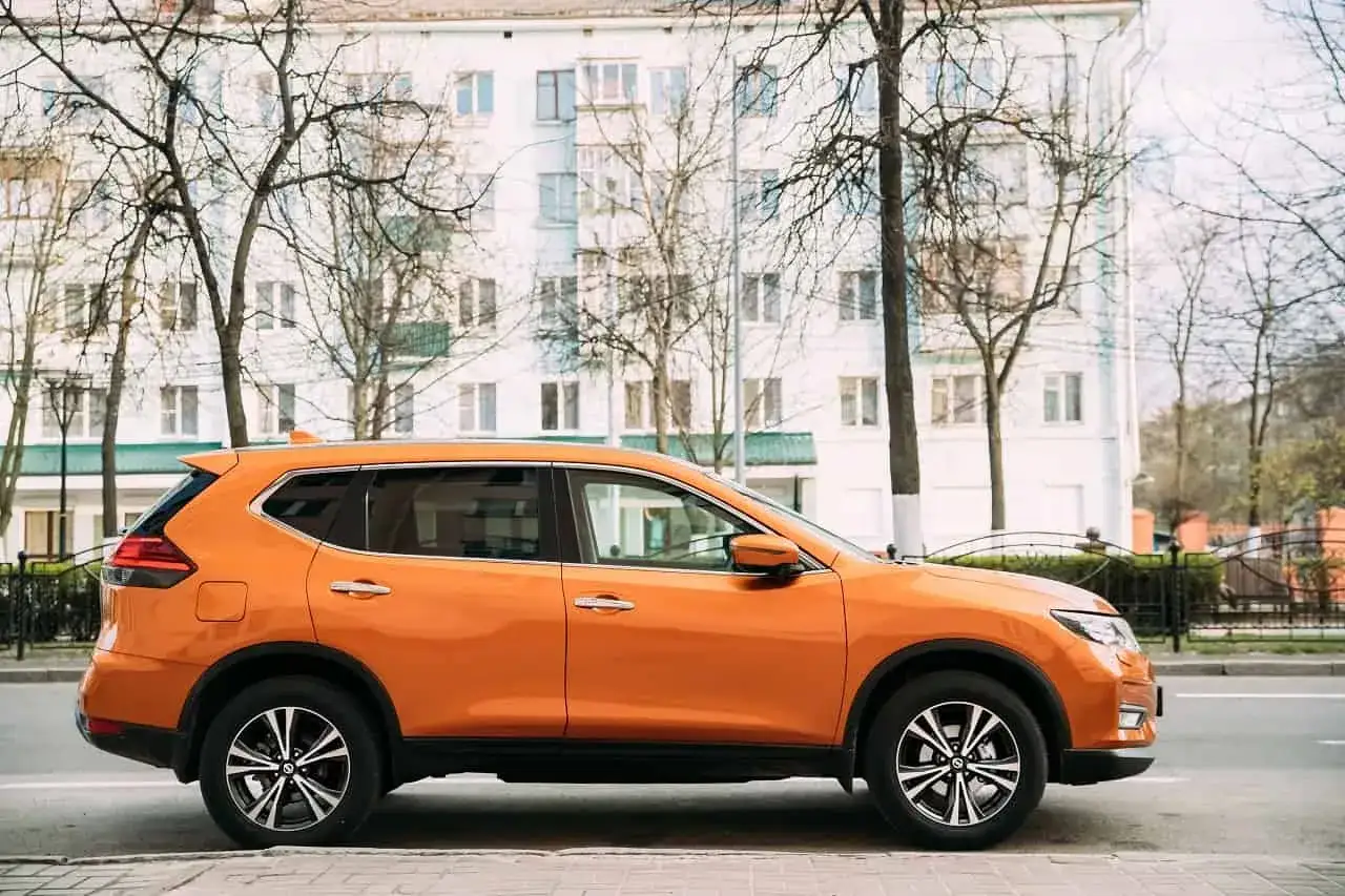 Pomarańczowy SUV do 70 tys. zaparkowany na tle białego budynku i drzew.