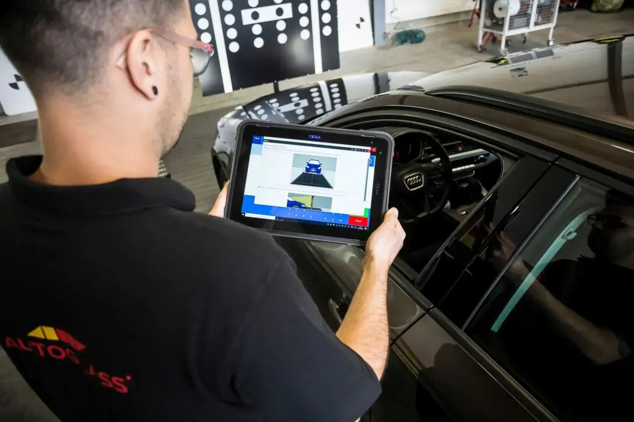 Technik z tabletem sprawdza kalibrację kamery ADAS, kluczową dla działania systemów wspomagających kierowcę, co jest częścią procesu związanego z ubezpieczeniem szyby w aucie.