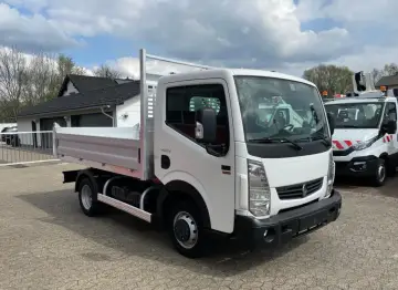 Biały Renault Maxity z otwartą skrzynią ładunkową stoi na placu. W tle budynek i inne pojazdy.