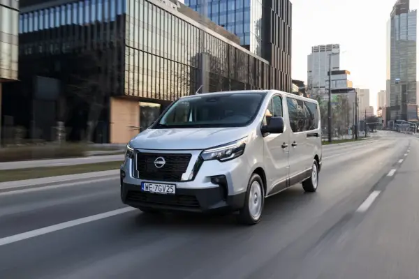 Srebrny van Nissan, jeden z najnowszych nissan modele, jedzie ulicą w nowoczesnym mieście.