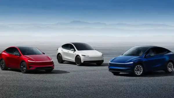 Trzy samochody Tesla: czerwony, biały i niebieski, stoją na pustej drodze z górami w tle.