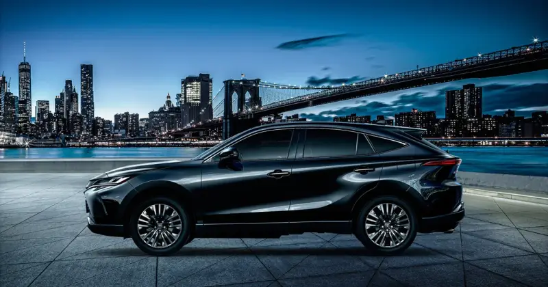Elegancki, czarny Toyota Harrier lśni nocą na tle rozświetlonego miasta i mostu.