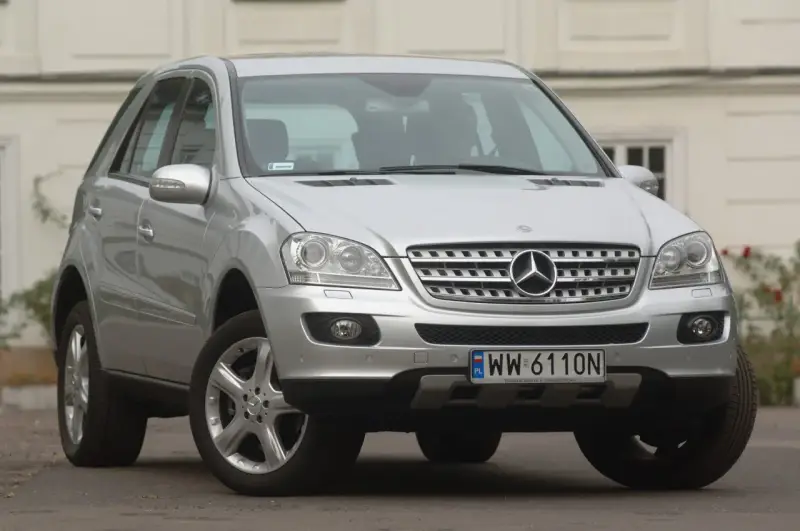 Srebrny Mercedes ML 320 z polskimi tablicami rejestracyjnymi WW 6110N zaparkowany przed budynkiem.
